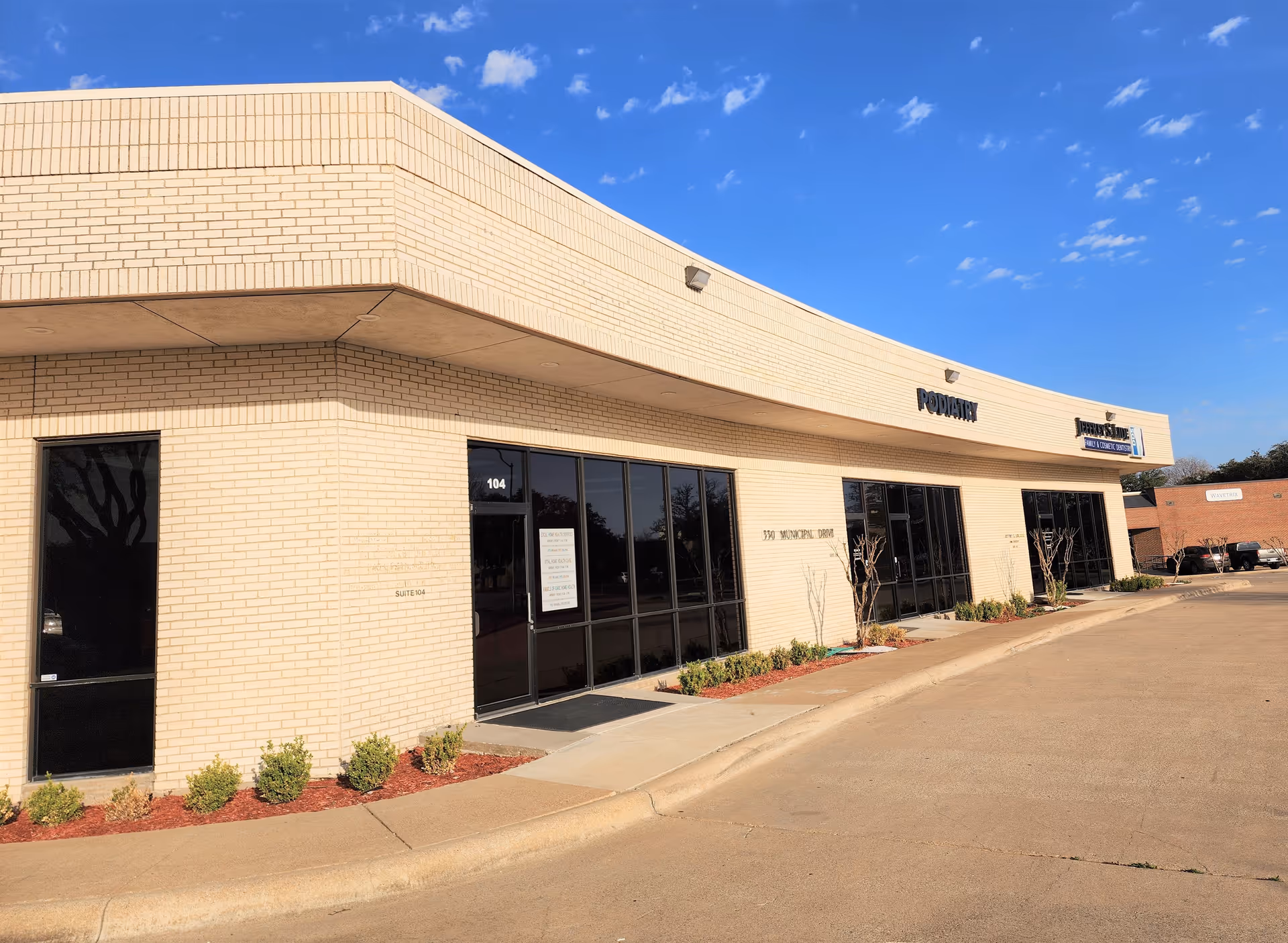 Beige brick Angels of Care Home Health, Inc building with curved façade, glass storefronts, and parking.