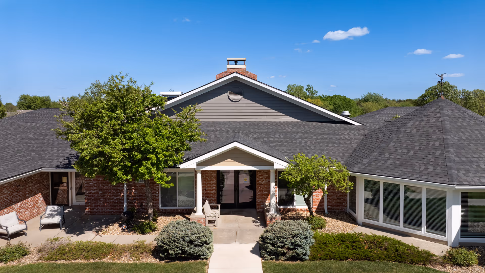 Single-story brick assisted living building with a central entrance and surrounding trees.