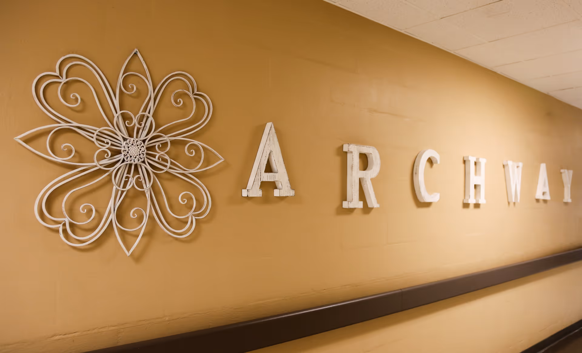 A beige wall with decorative white metal flower art and large white letters spelling 'ARCHWAY'.