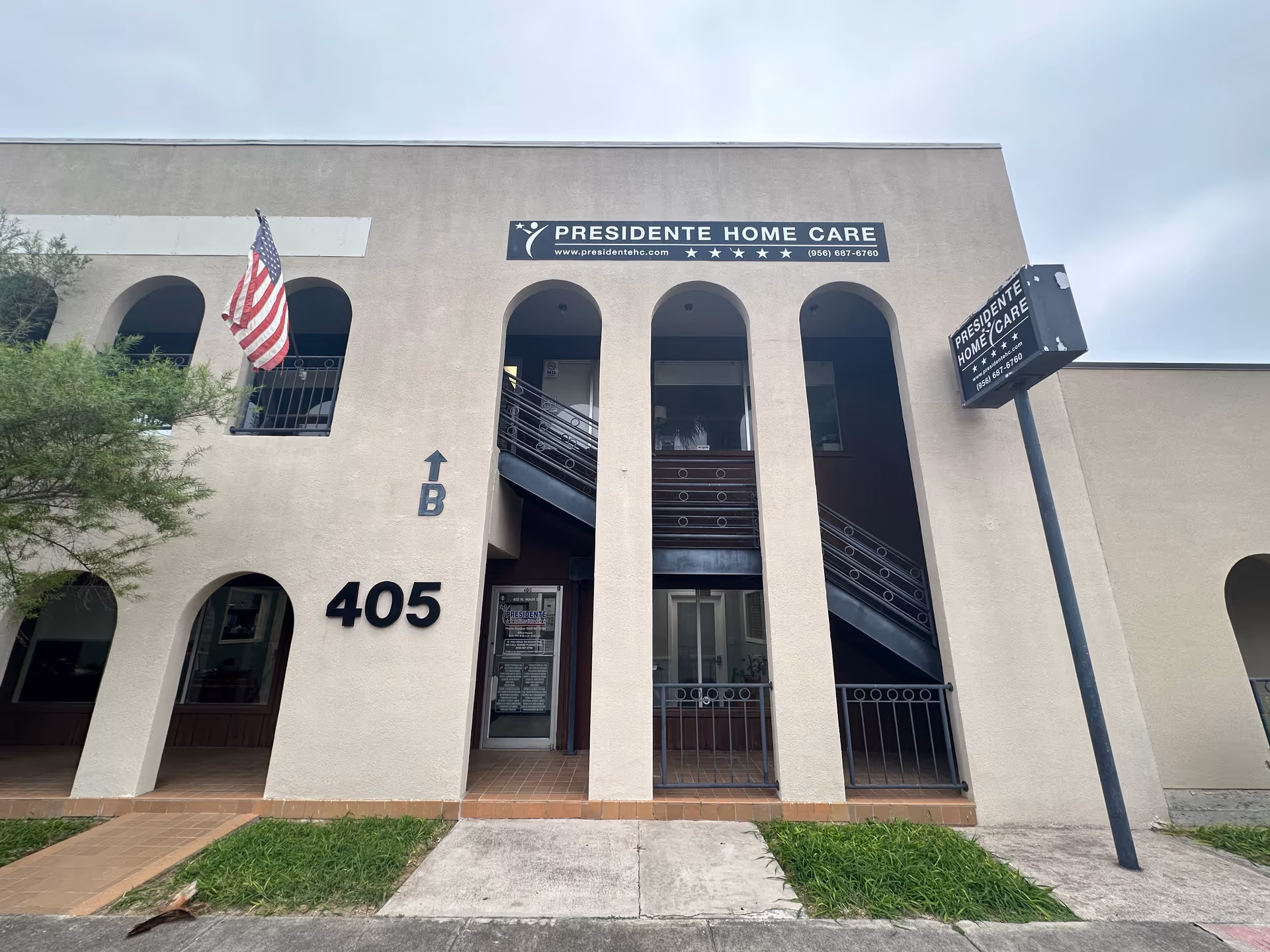 Beige building front with arches, Presidente Home Care sign, address 405, and American flag.