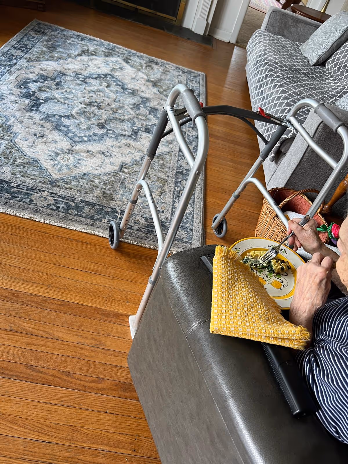 A walker beside a gray sofa while someone eats from a plate in the living room.