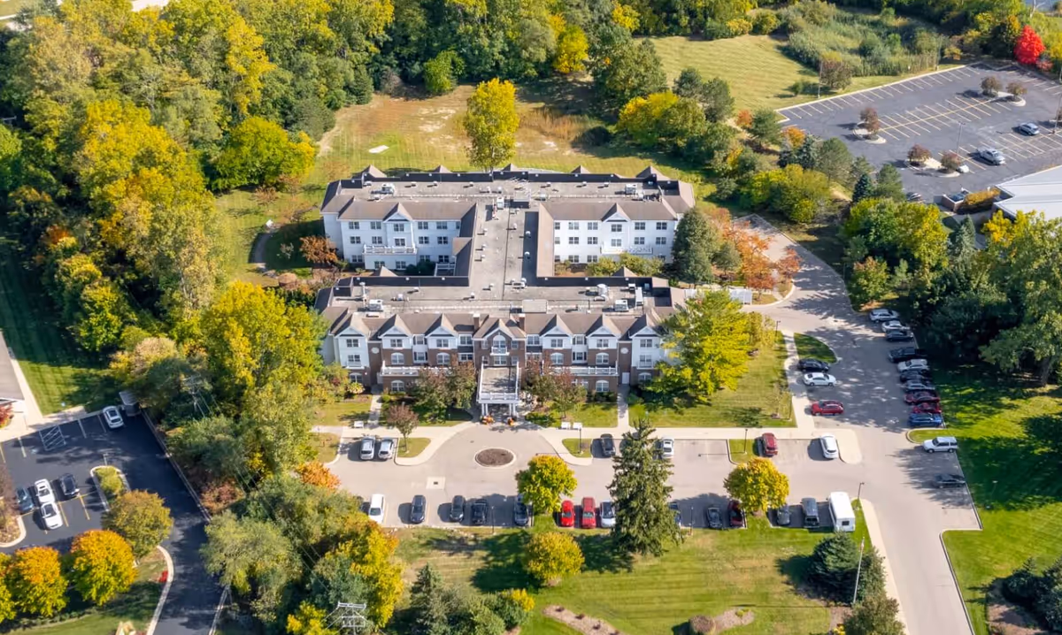 Aerial view of a multi-wing senior living building with a front entrance, parking lots, and surrounding trees and lawns.
