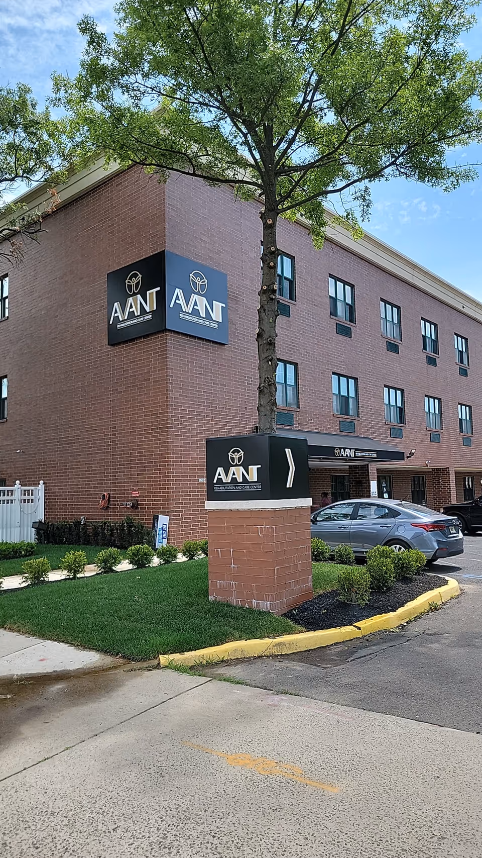 Brick exterior of Avant Rehabilitation and Care Center with signage, tree, and parked cars.