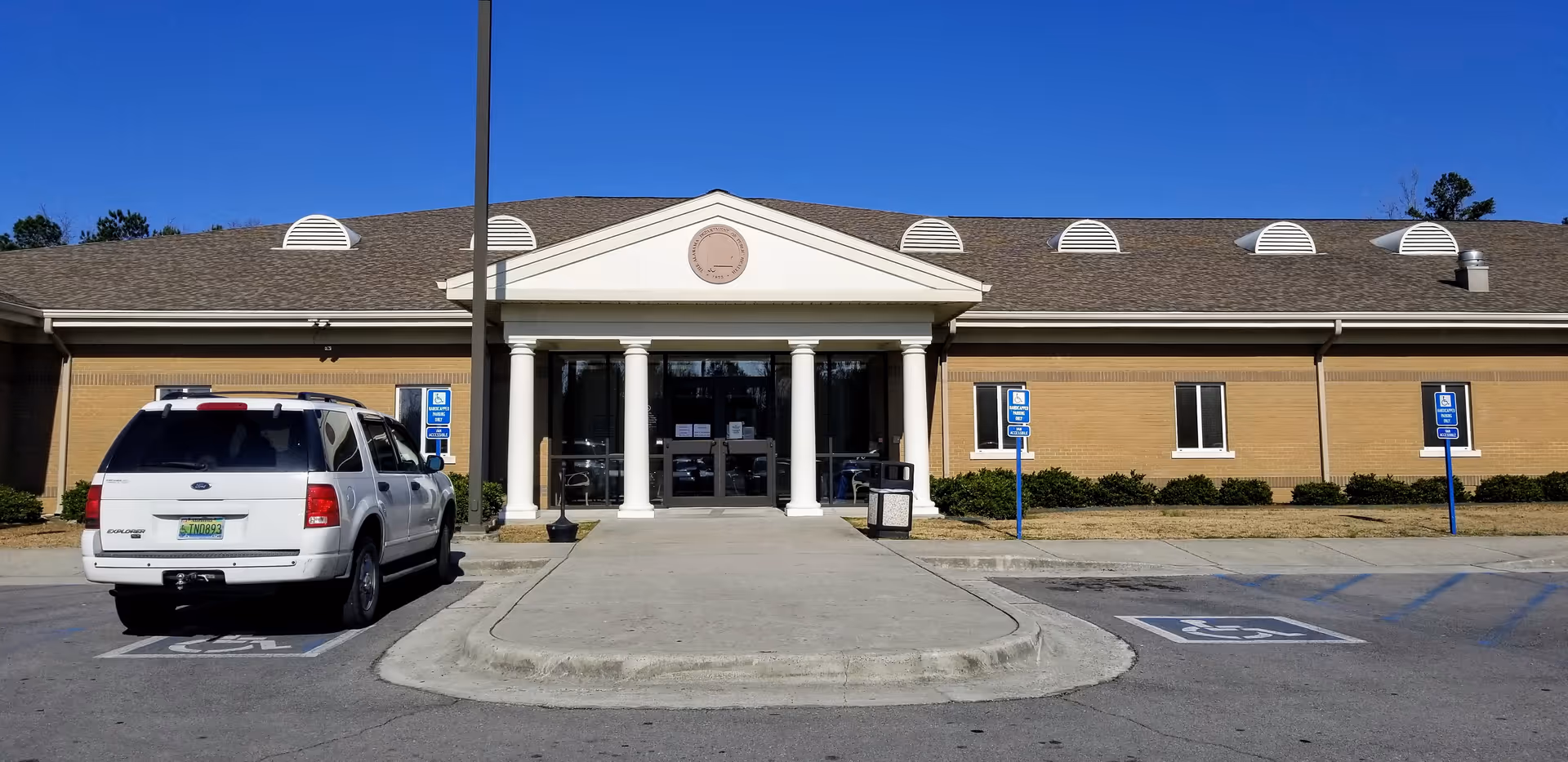 Front view of a brick health department building with columns and accessible parking.