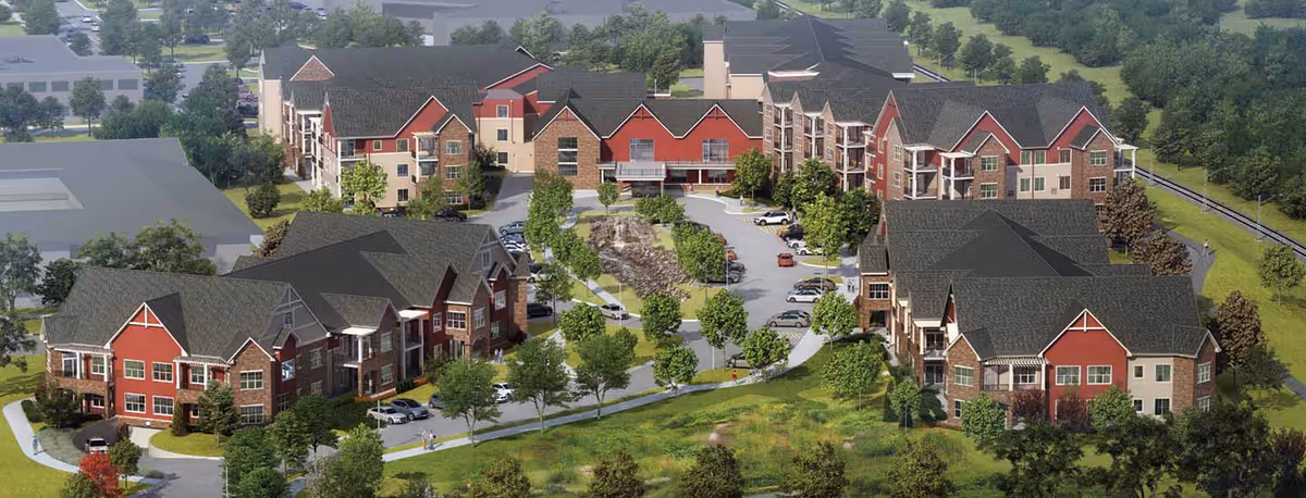 Aerial view of Founders Ridge senior living facility showing multiple multi-story residential buildings with red and beige exteriors, surrounded by trees, parking areas, and landscaped green spaces.