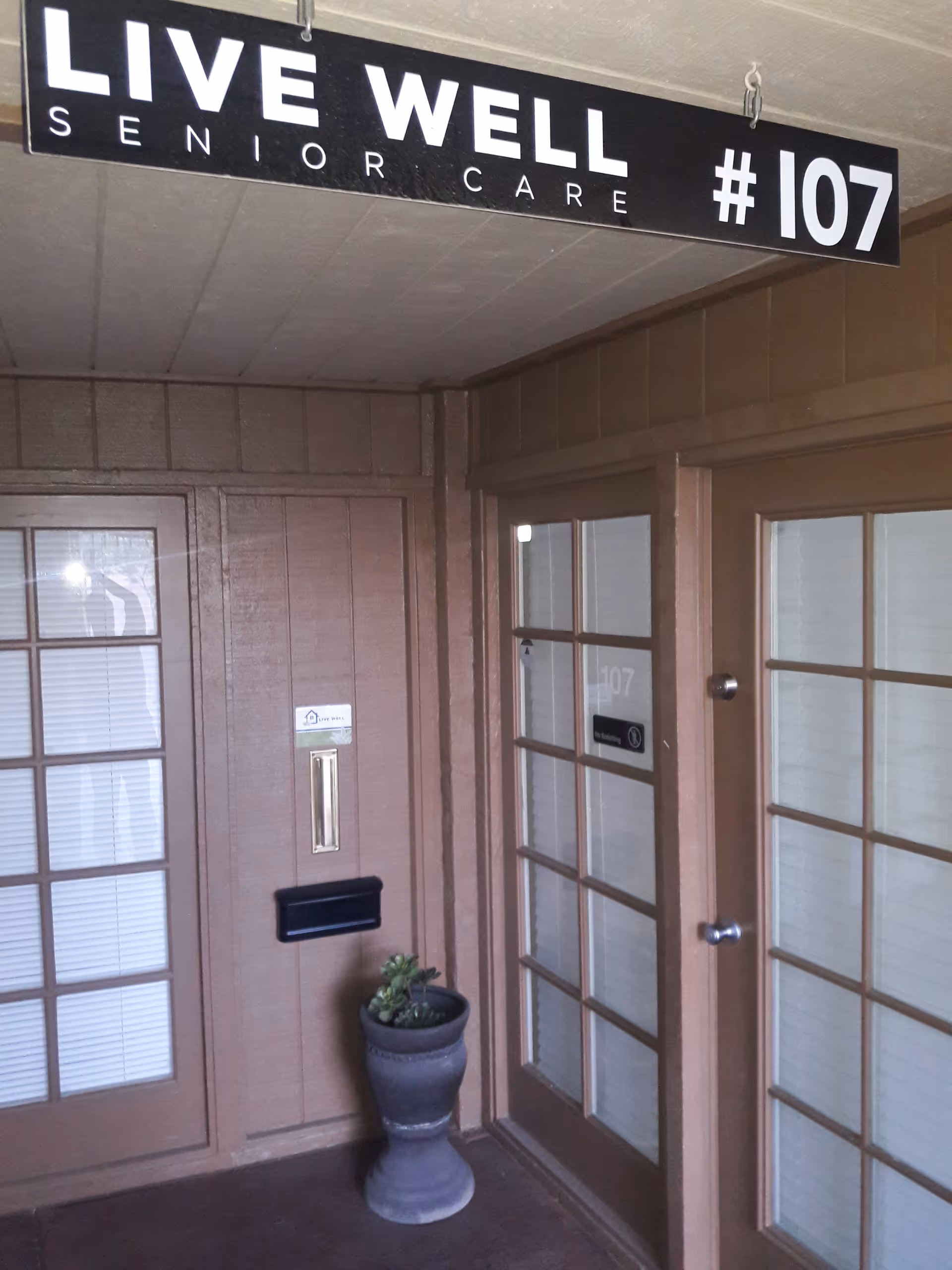 Indoor hallway entrance to unit 107 with a Live Well Senior Care sign and potted plant