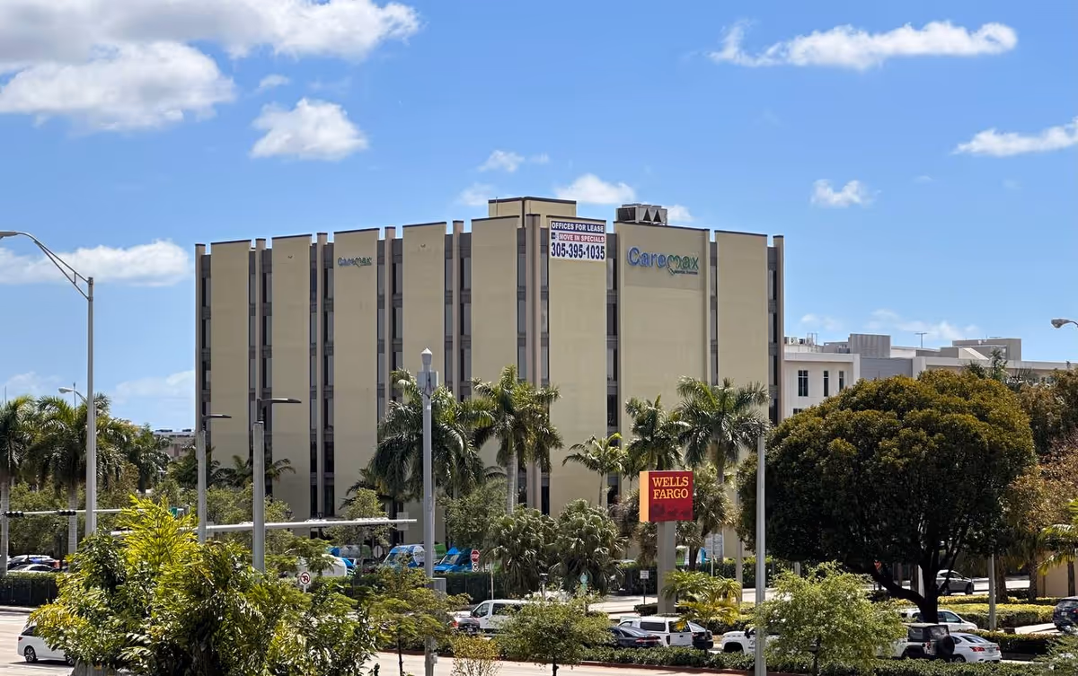 Exterior view of a tall beige medical building with palm trees and parked cars.