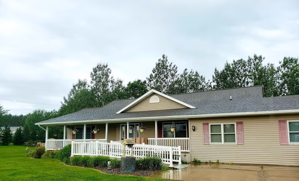 Front view of a single-story beige senior home with a white porch and manicured lawn.