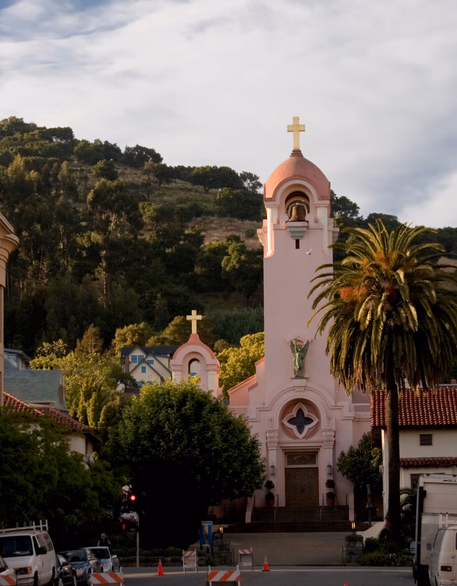 Pink church with bell tower and cross along a street with palm trees