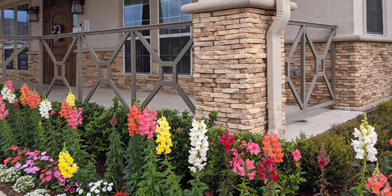 Front exterior of Evergreen Cottages Magnolia with stone columns, railing, and colorful flowers.