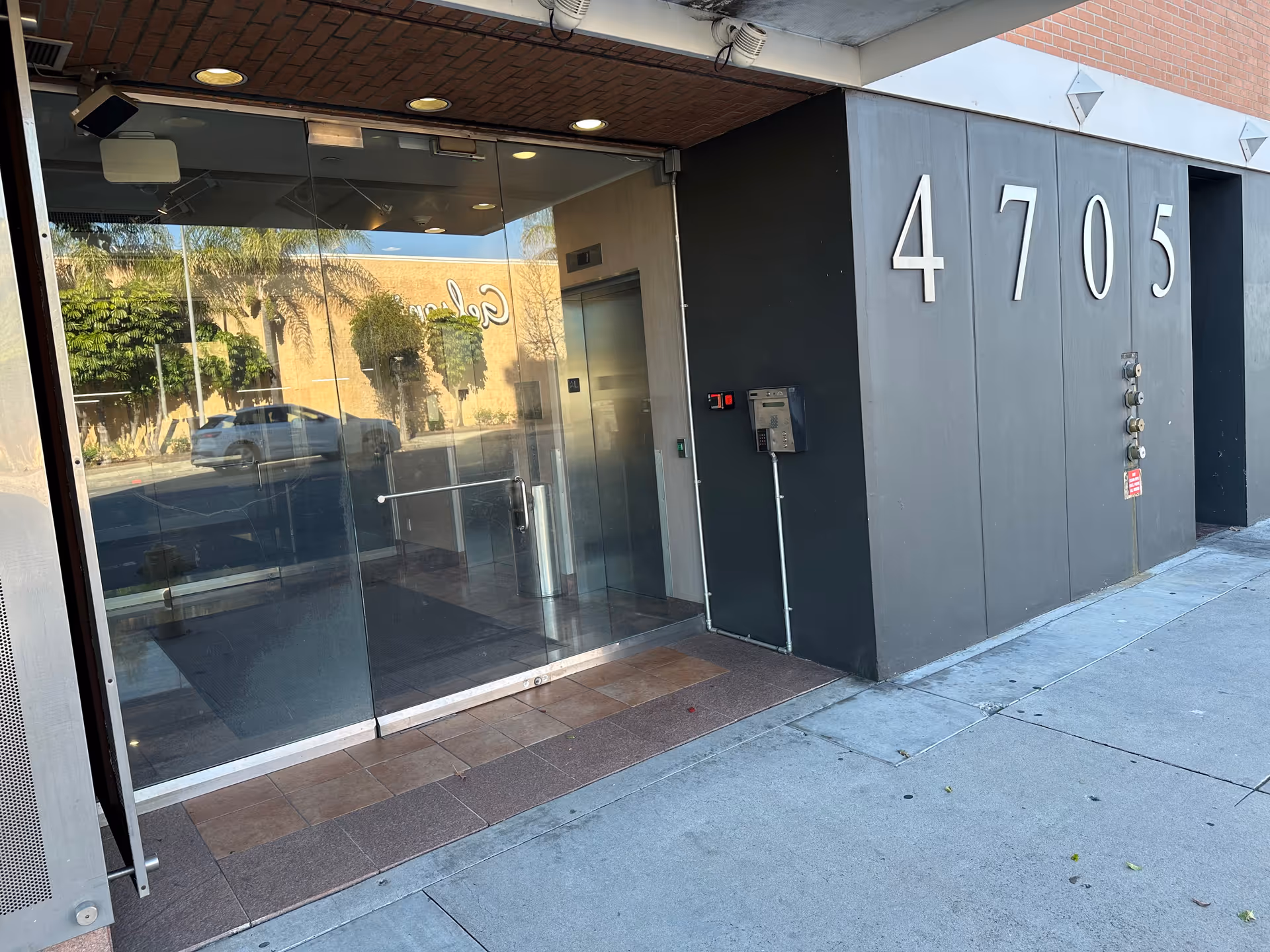 Glass entrance doors reflect street views while large white numbers 4705 decorate the dark building front.
