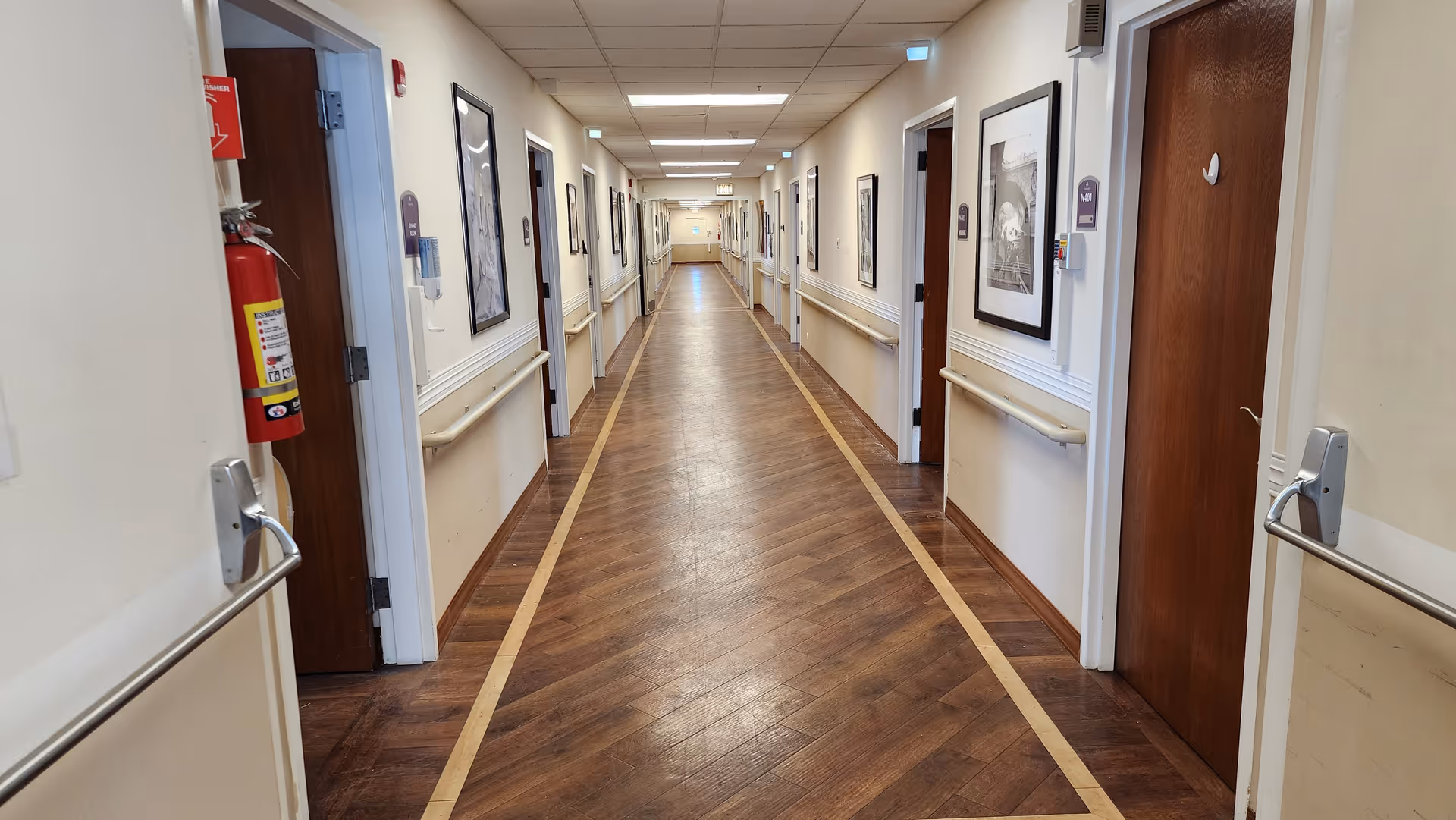 Long hallway in a senior living facility with doors, handrails, and framed art.