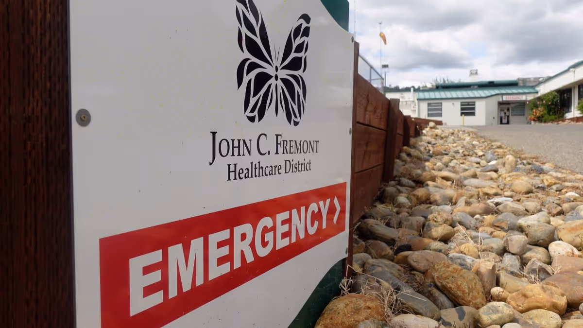 Sign shows John C. Fremont Healthcare District with a large Emergency arrow beside a rocky path