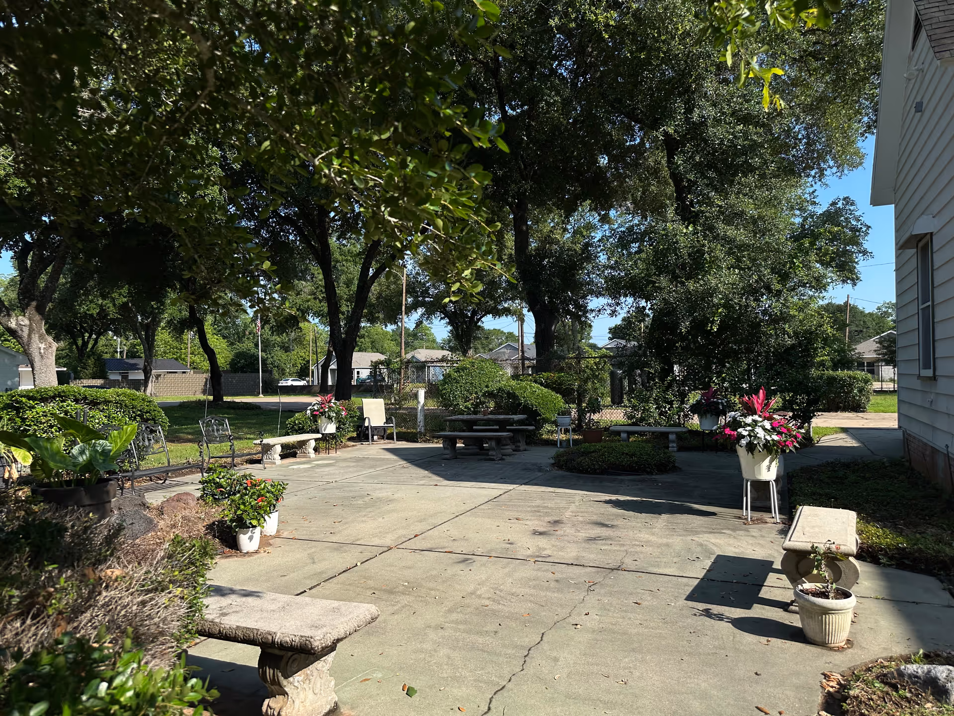 Shaded outdoor courtyard with benches, planters, and trees beside a light building.