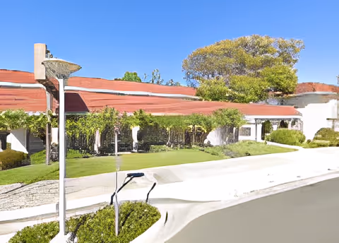 Low-rise senior living building with a red tile roof, covered walkway and landscaped front lawn under a clear blue sky.