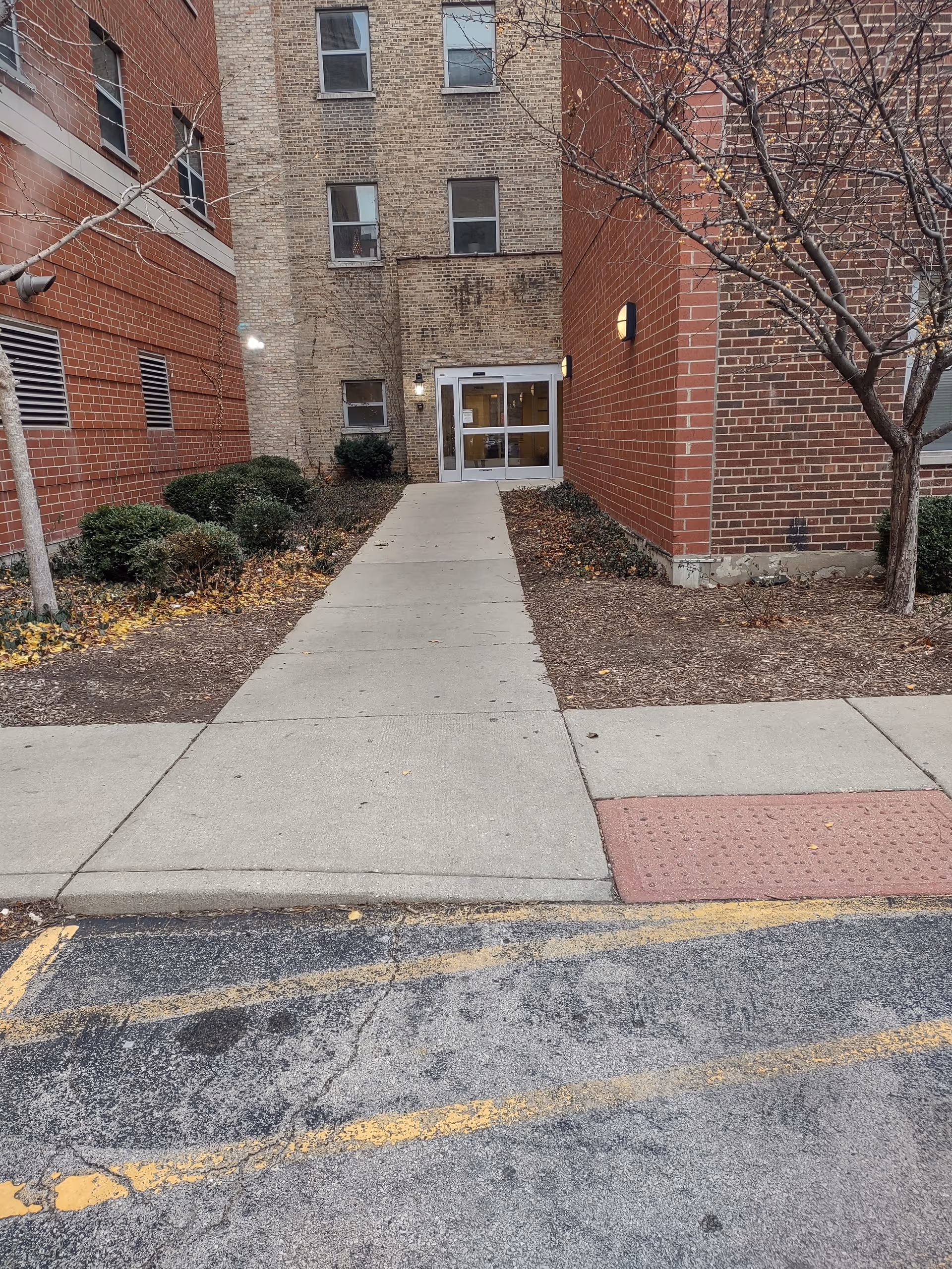 Exterior view of a brick senior living building with a central walkway leading to glass doors.