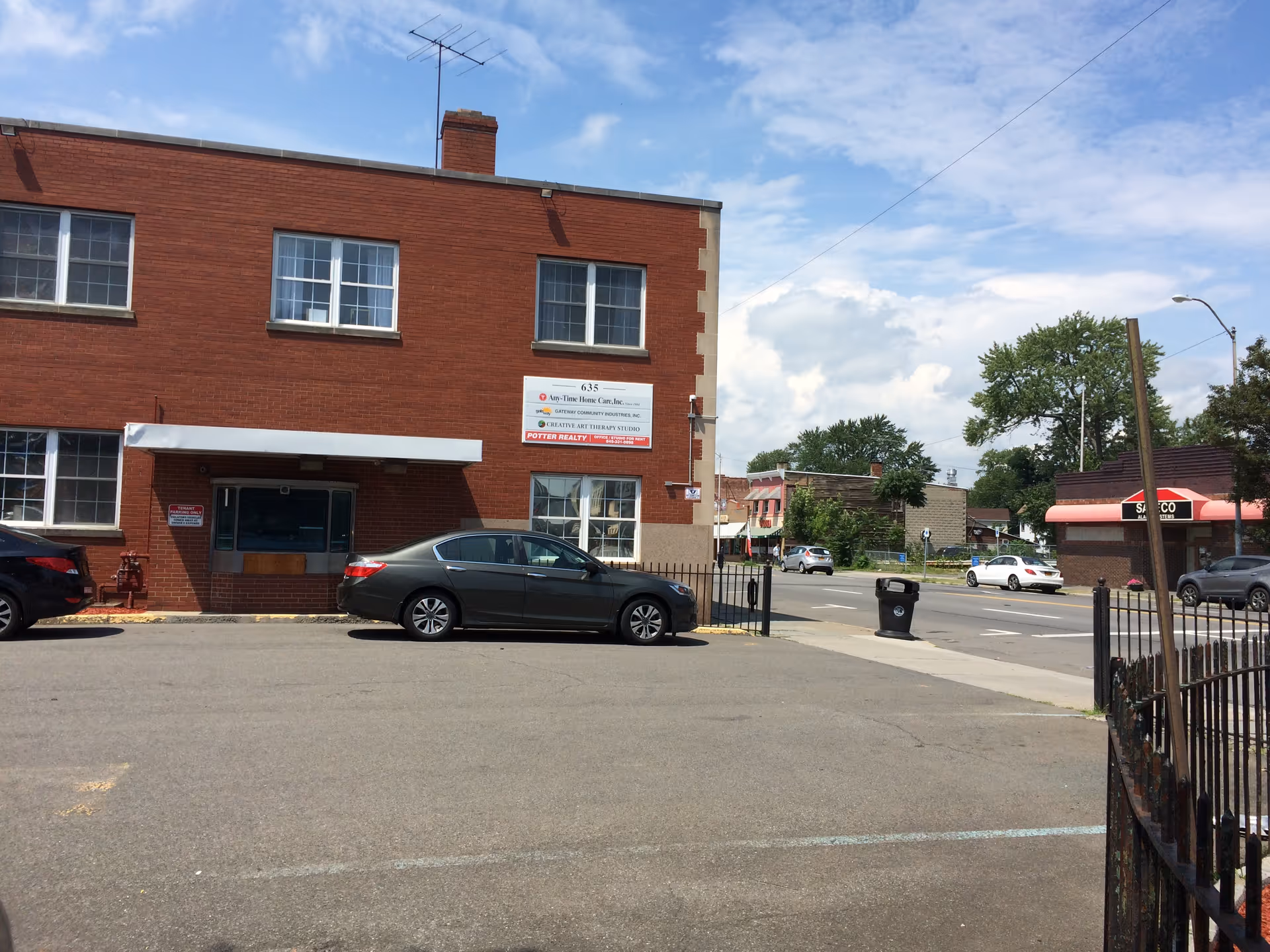 Red brick two-story building with Any-Time Home Care Inc sign and parked cars outside