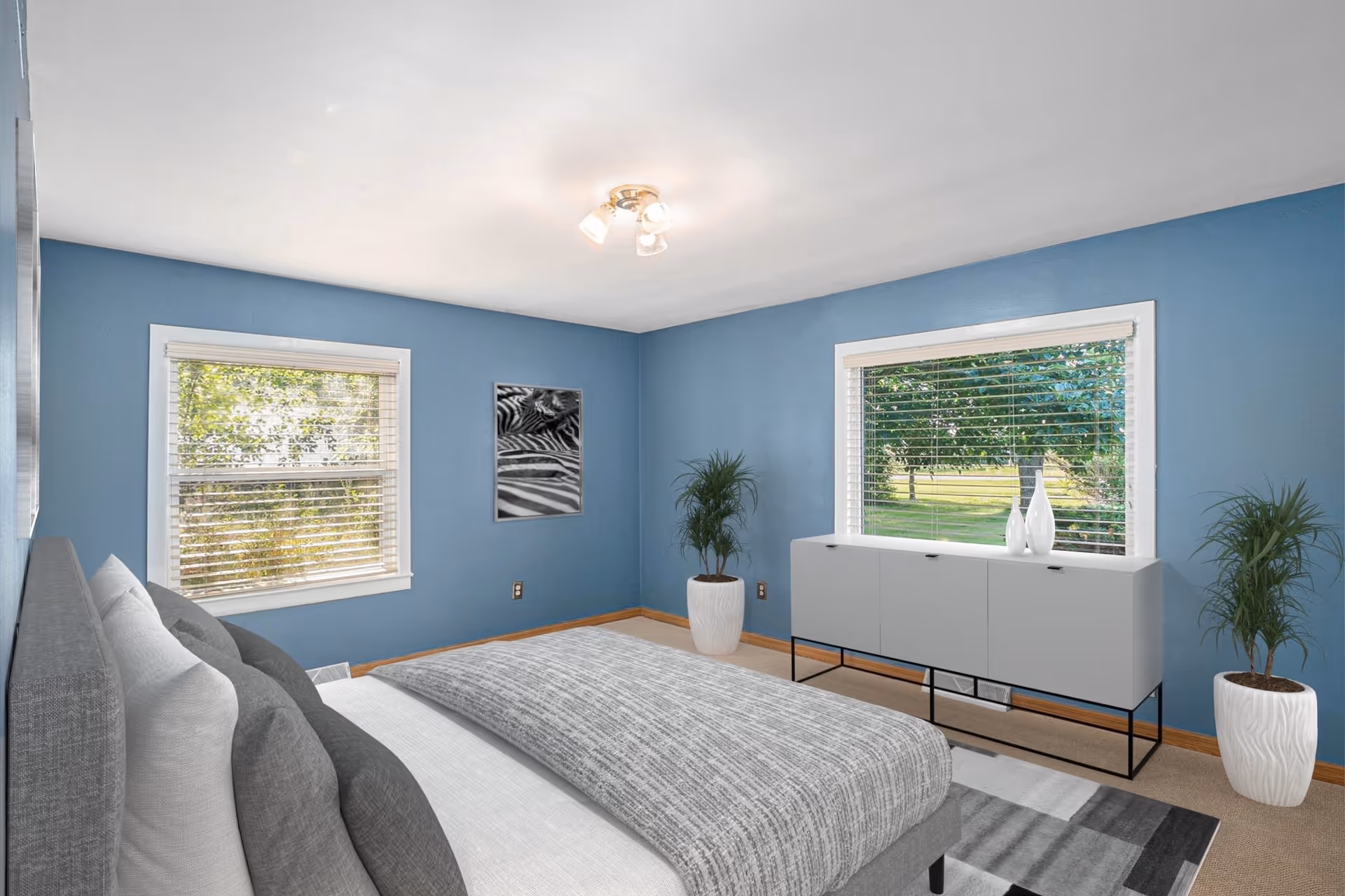 Blue-walled bedroom with a bed, dresser, two windows, and potted plants.