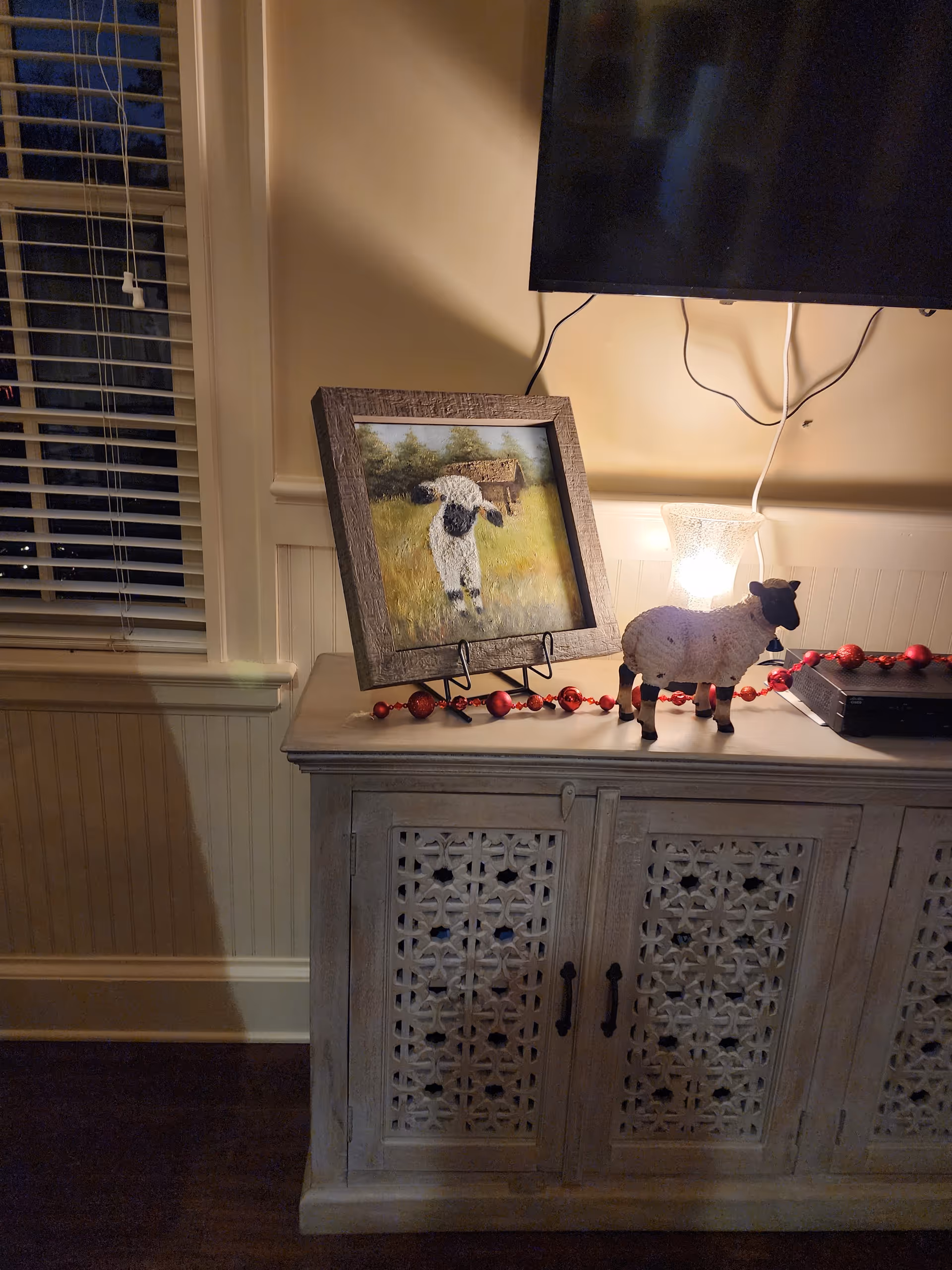 A cozy living room scene with a carved cabinet, framed sheep painting, and decorative sheep figure.