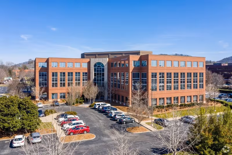 Brick senior living facility with central arched entrance and surrounding parking lot.
