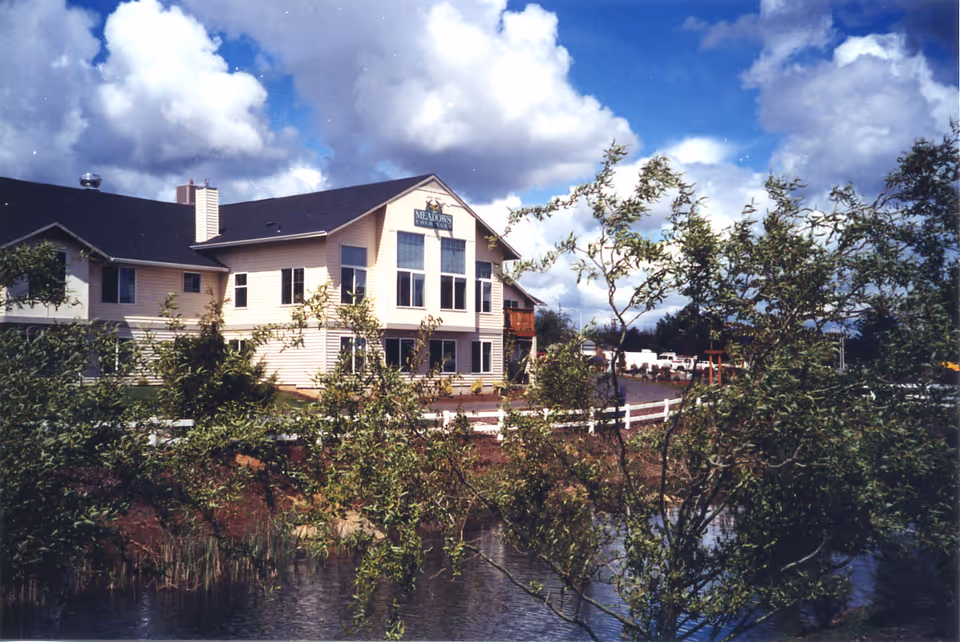 Front view of Meadows Courtyard senior living facility with a pond and trees.