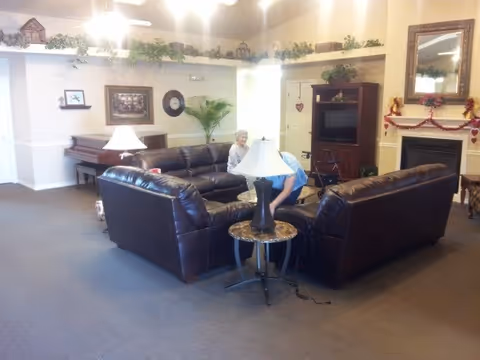 Common living room in a senior facility with leather sofas, lamps, piano, and residents.