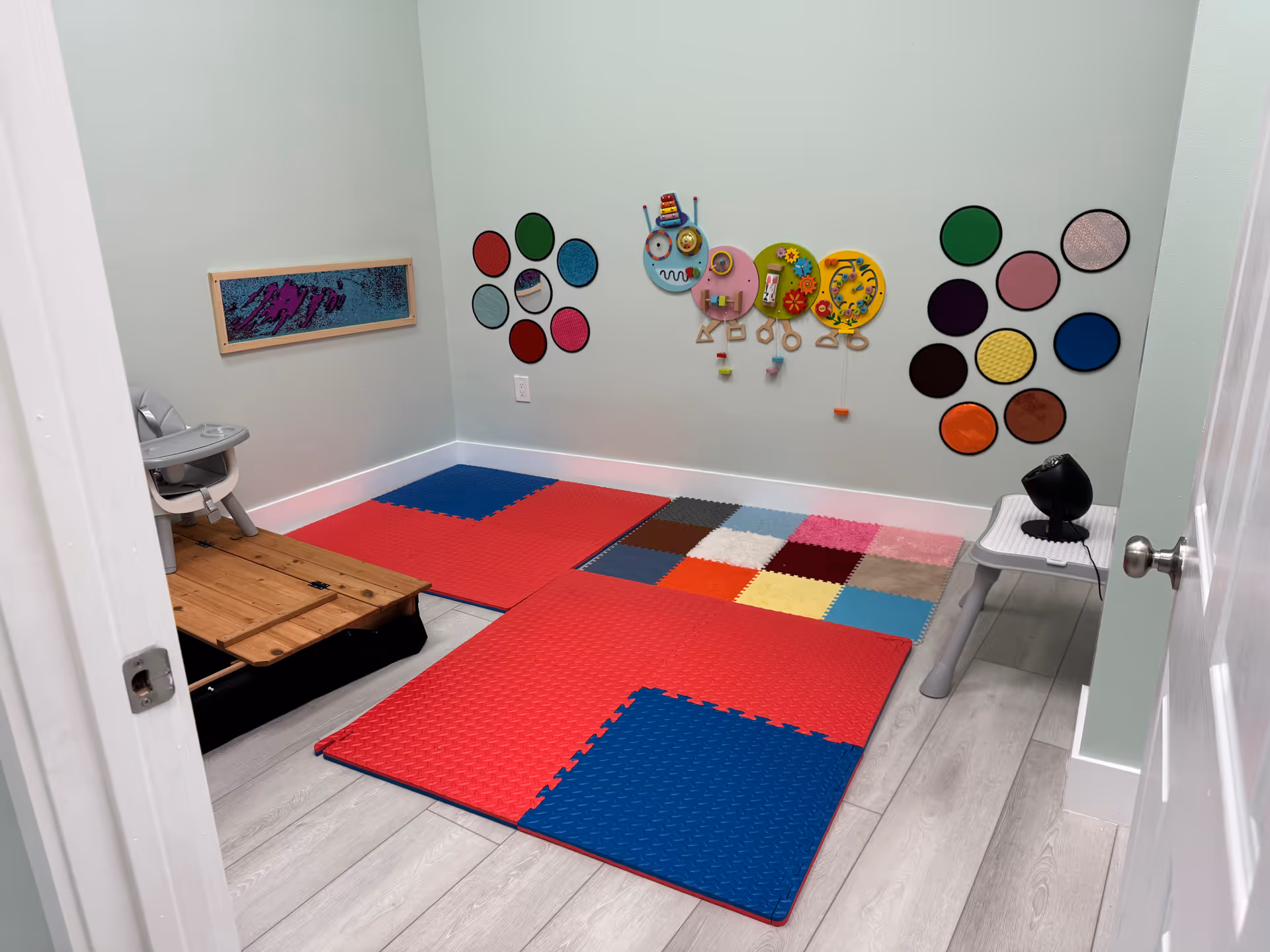 Interior therapy playroom with red-blue foam mats and colorful circular wall decorations.