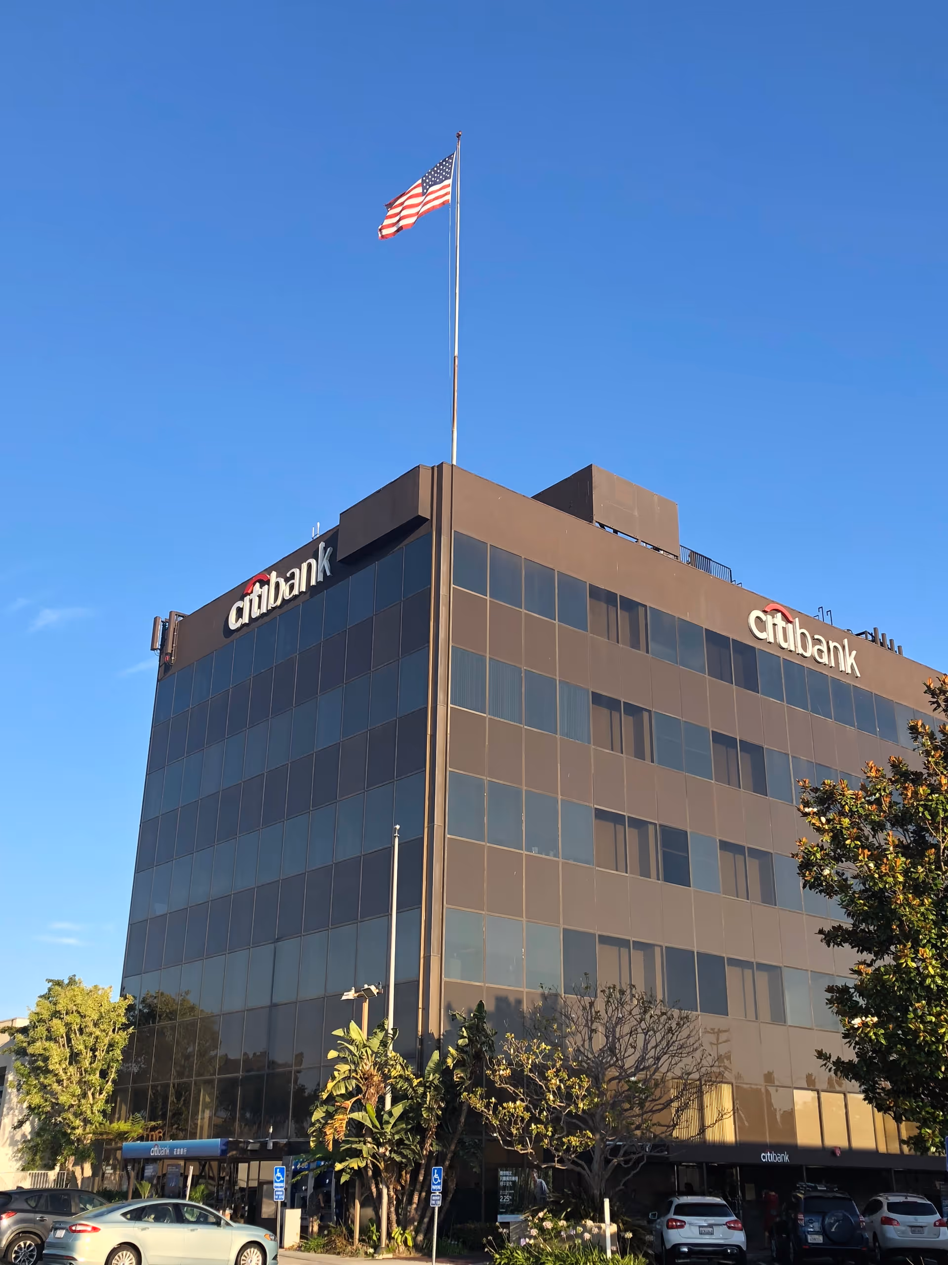 Tall glass office building with a flag at the top and CitiBank logos.