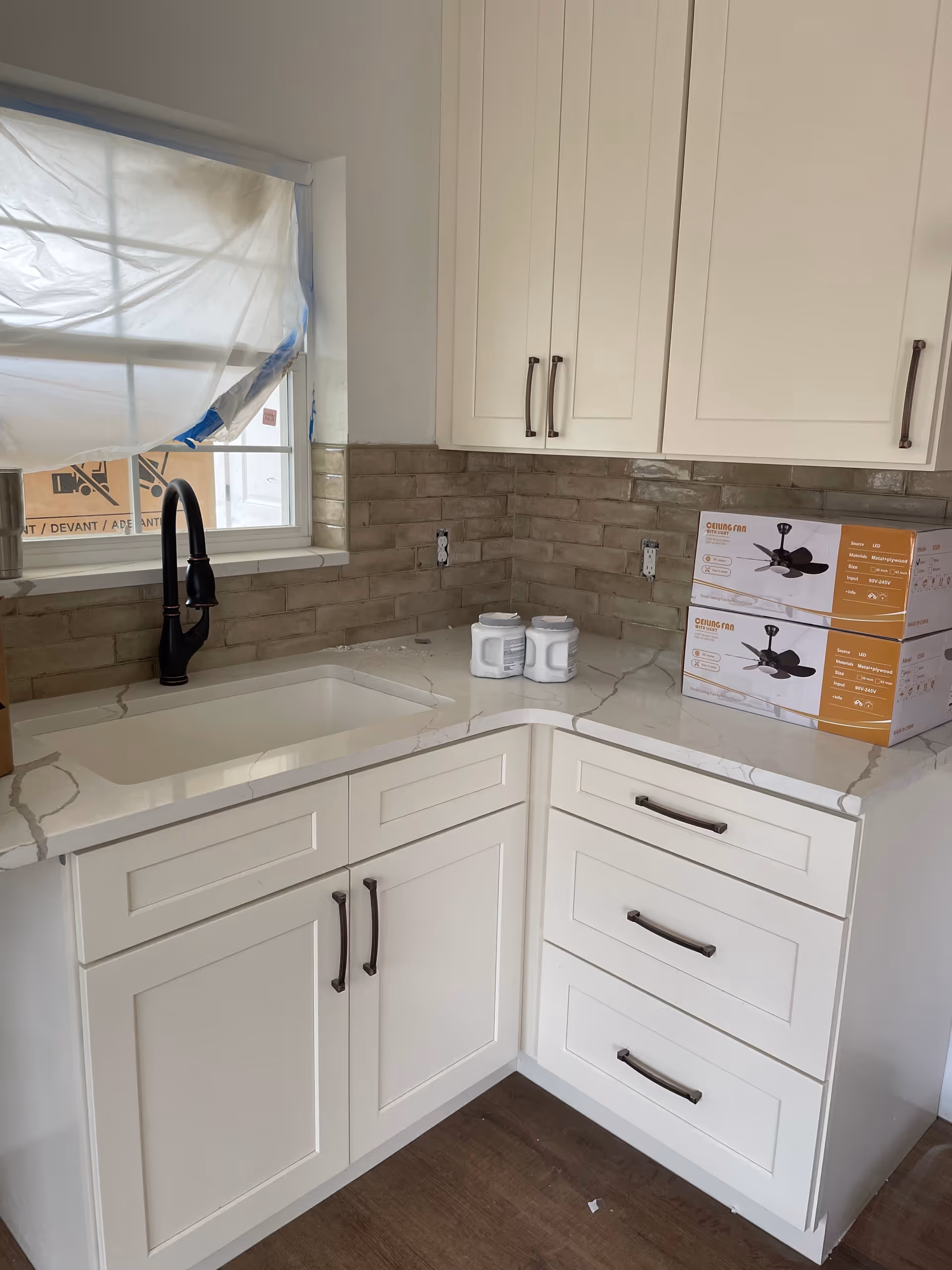 White kitchen cabinets and sink with a beige tile backsplash and boxed products on the counter