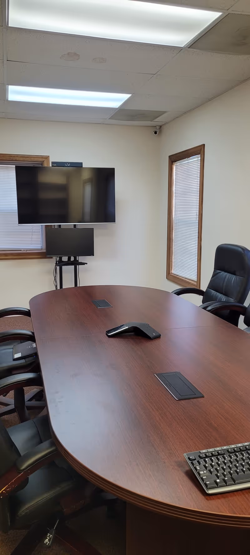 Empty conference room with curved wooden table, chairs, and wall-mounted monitors.