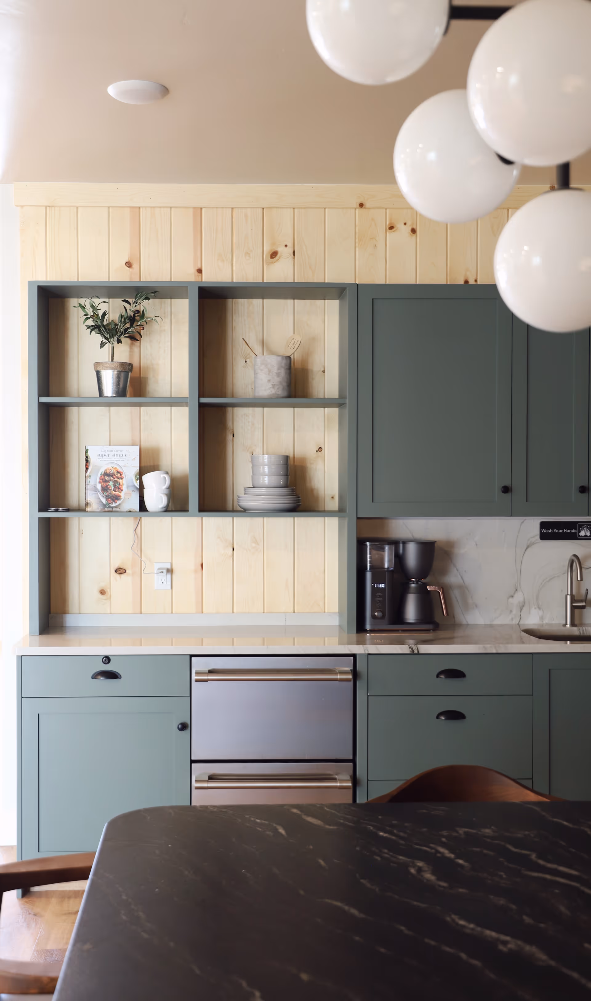 Open-concept kitchen with sage green cabinets, open shelves, coffee maker, and a marble tabletop.