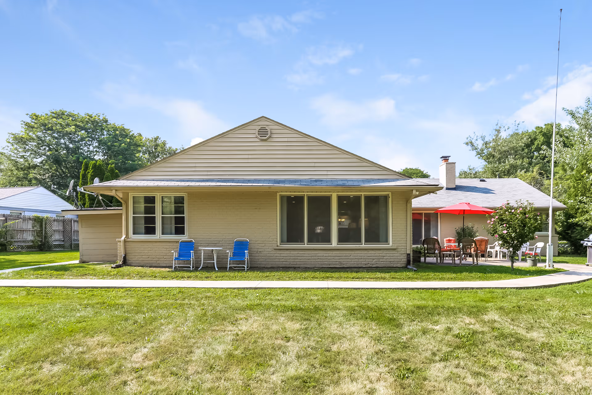 Single-story beige brick facility front with lawn, blue chairs, and a red umbrella patio.