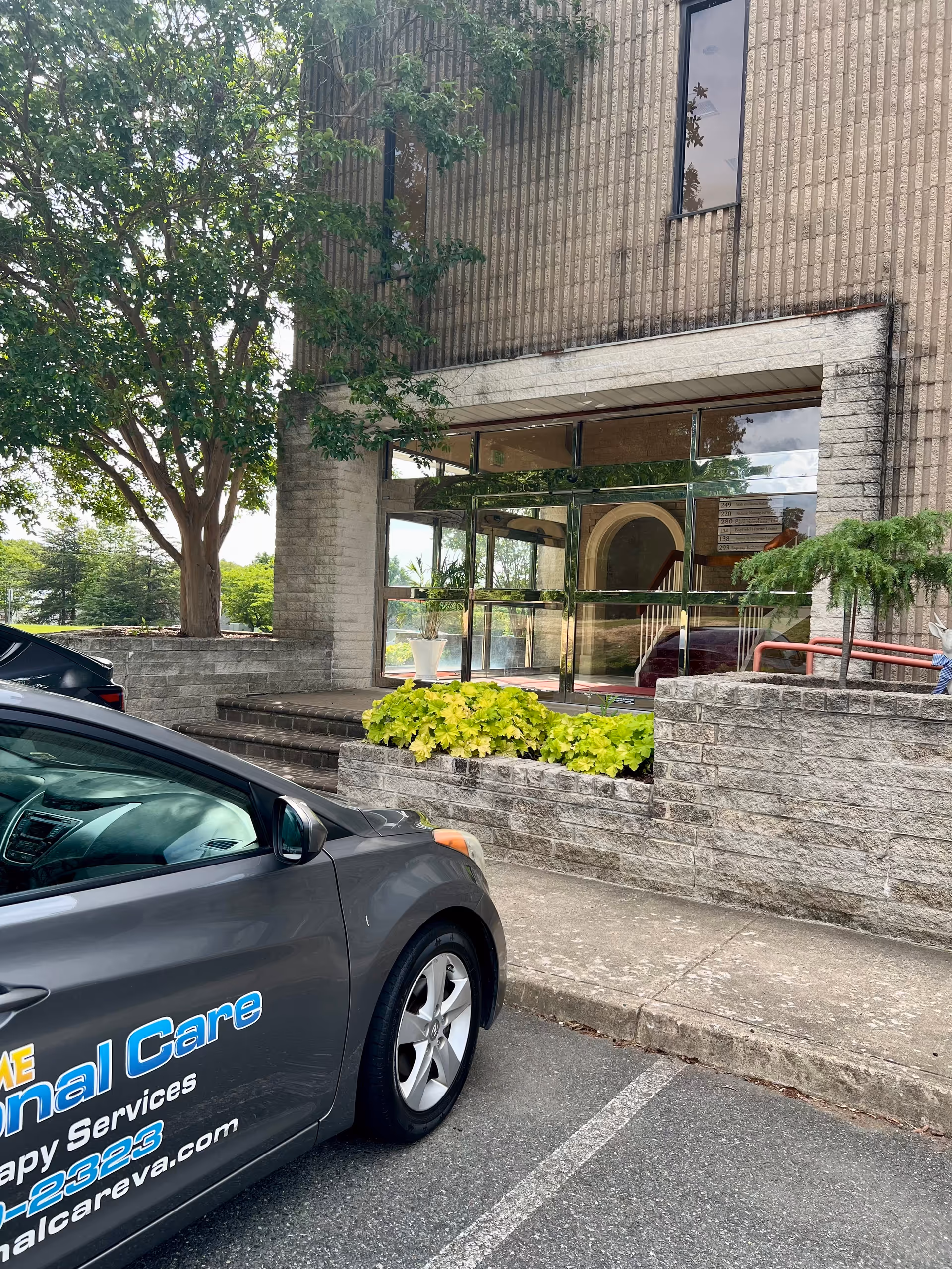 Exterior view of a facility entrance with glass doors, stone facade, and a parked car.