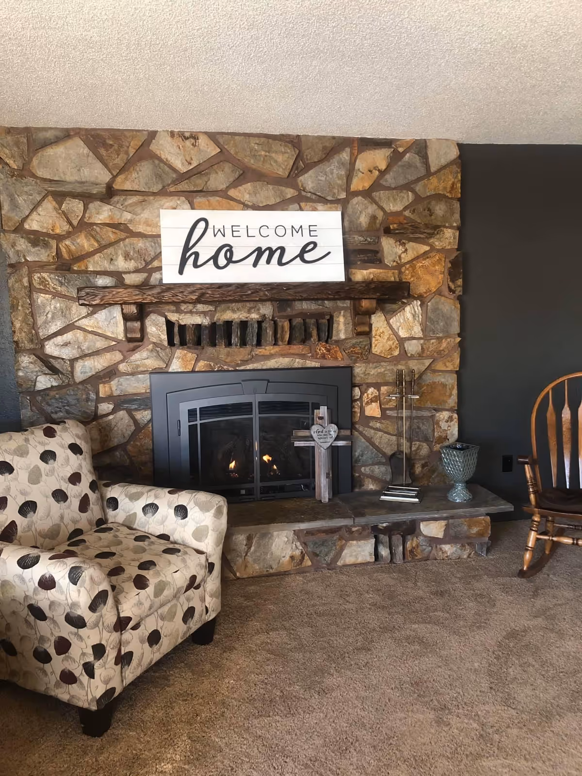 Stone fireplace with a wooden mantle and a Welcome home sign in a cozy living room.