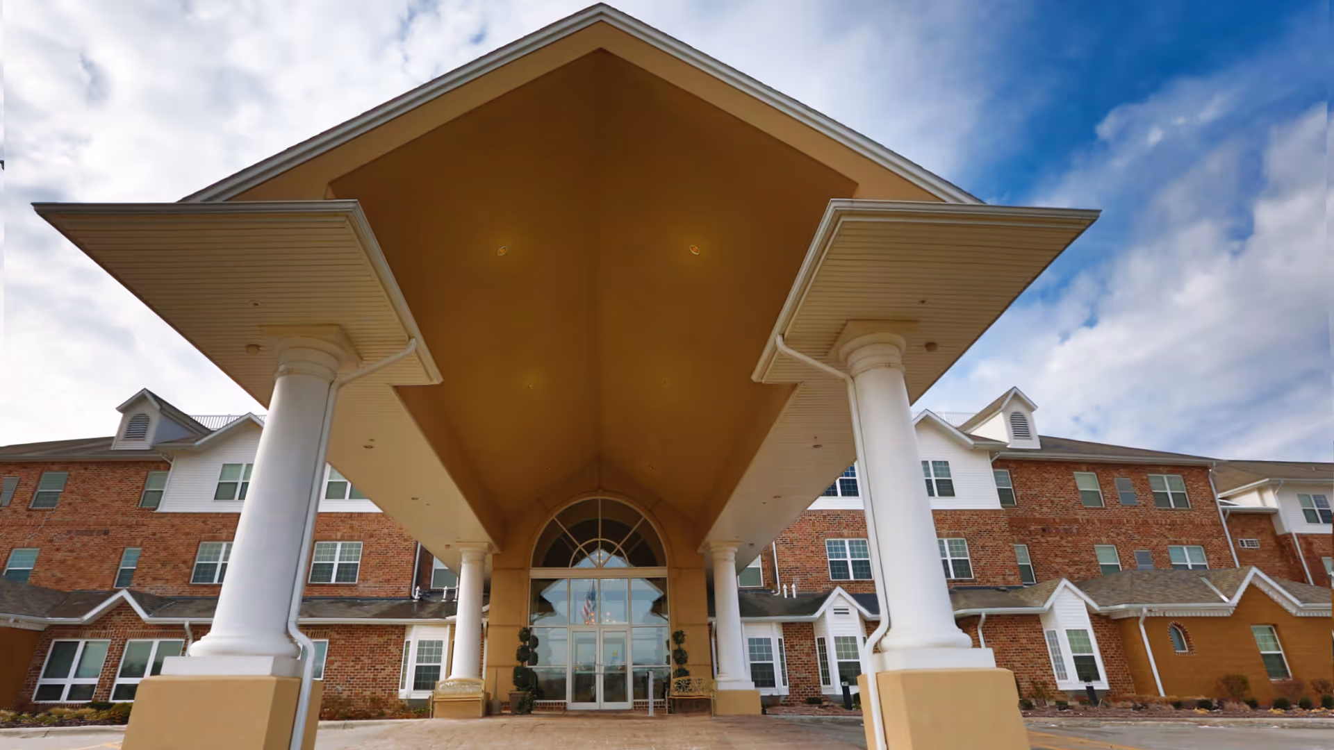 Front exterior view of Maple Ridge Retirement Community with brick building and covered entrance.