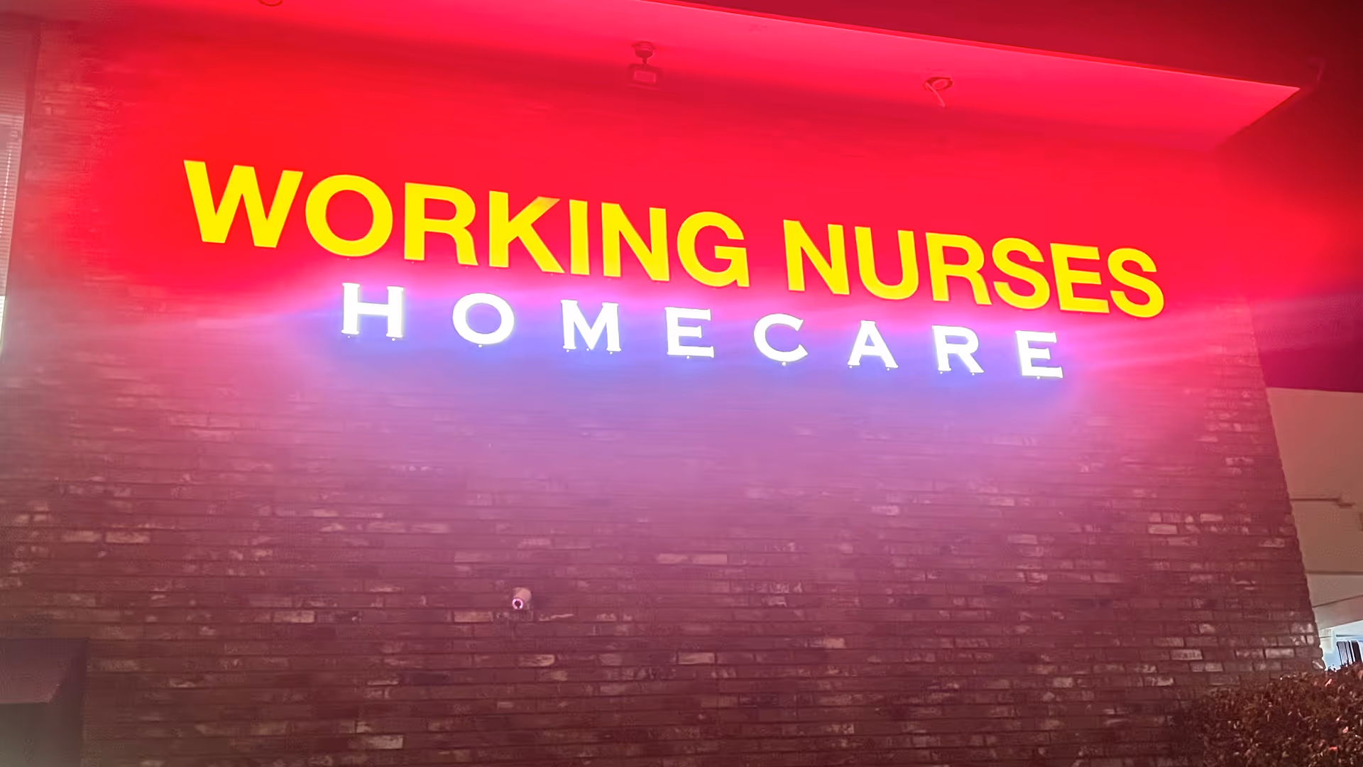Neon sign reading WORKING NURSES HOMECARE on a brick wall.