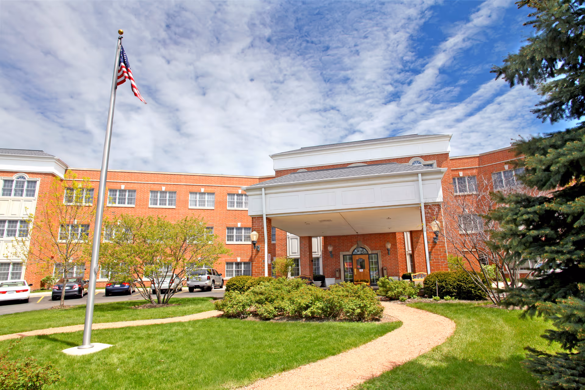 Brick senior living facility exterior with flagpole, driveway, and landscaped entrance.