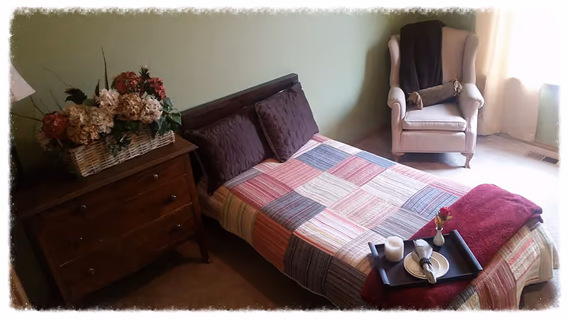 A cozy bedroom with a bed, dresser, and seating in a senior living setting.