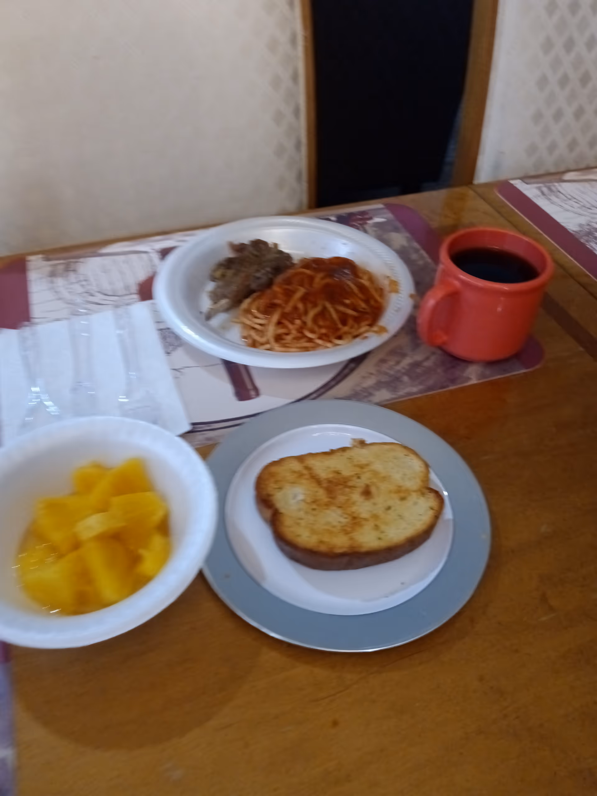 Table with pasta, bread slice, fruit, and coffee mug on placemats.
