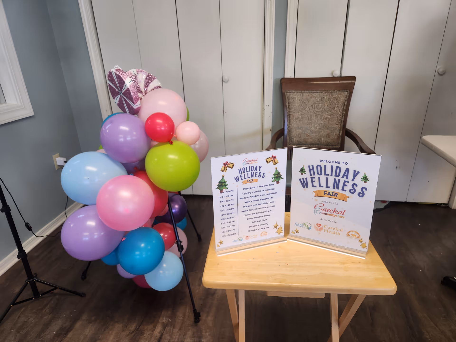 Indoor facility room with colorful balloons, a wooden table, and wellness fair signs.