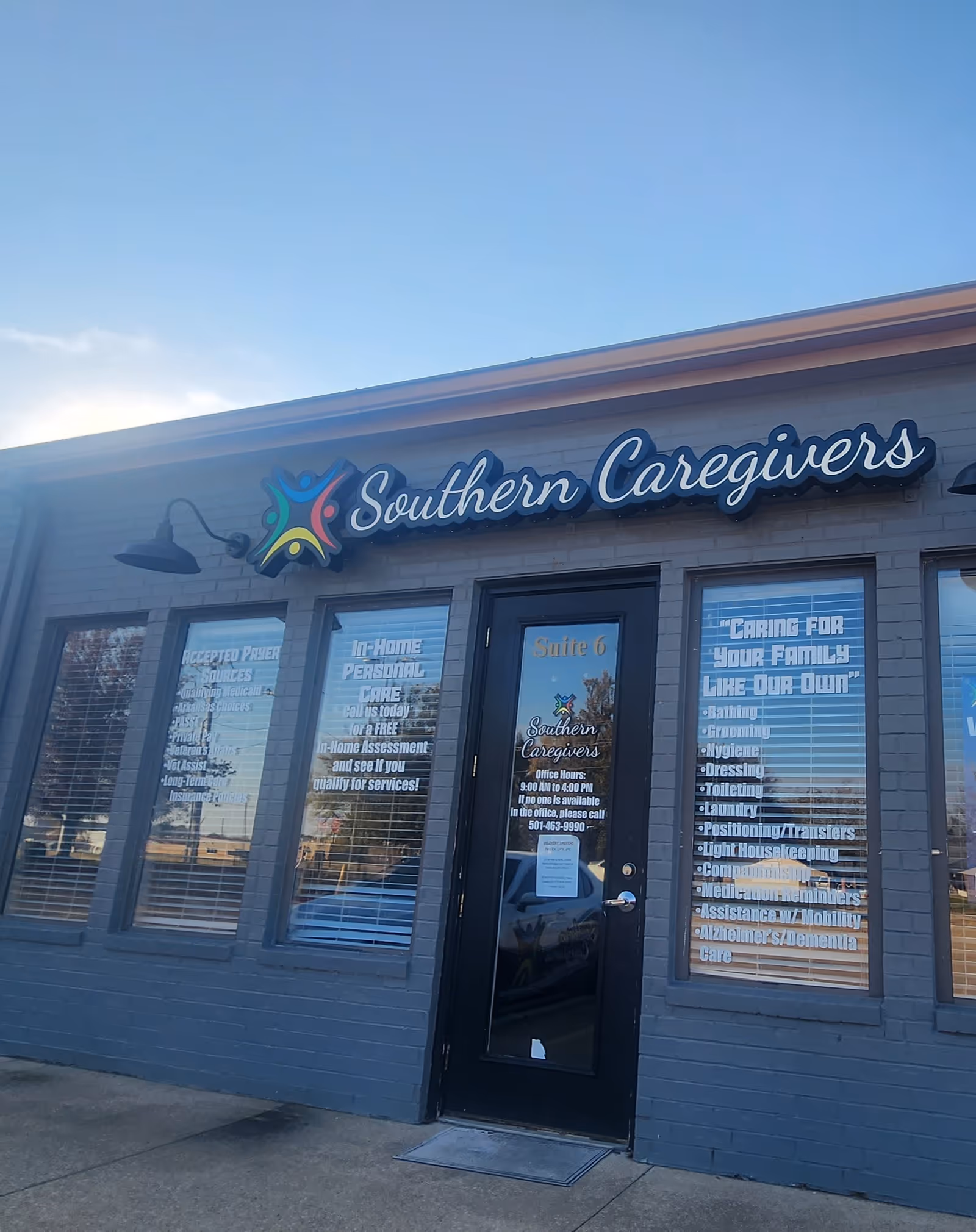 Blue-gray building front with Southern Caregivers sign, windows listing services and a black entrance door.