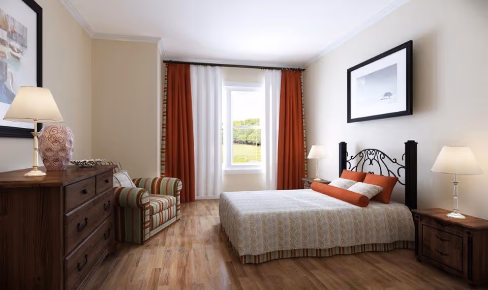 A warmly lit bedroom with a large bed, iron headboard, wooden dresser, and striped seating.