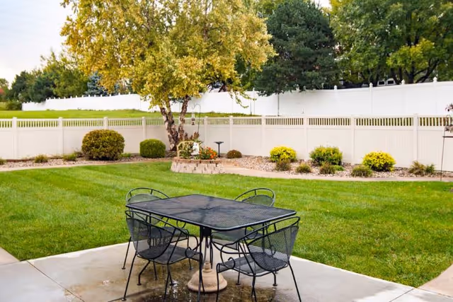 Metal outdoor dining table with chairs on a grassy backyard patio.