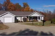 Single-story building with attached garage, front lawn, driveway, and autumn trees in background.