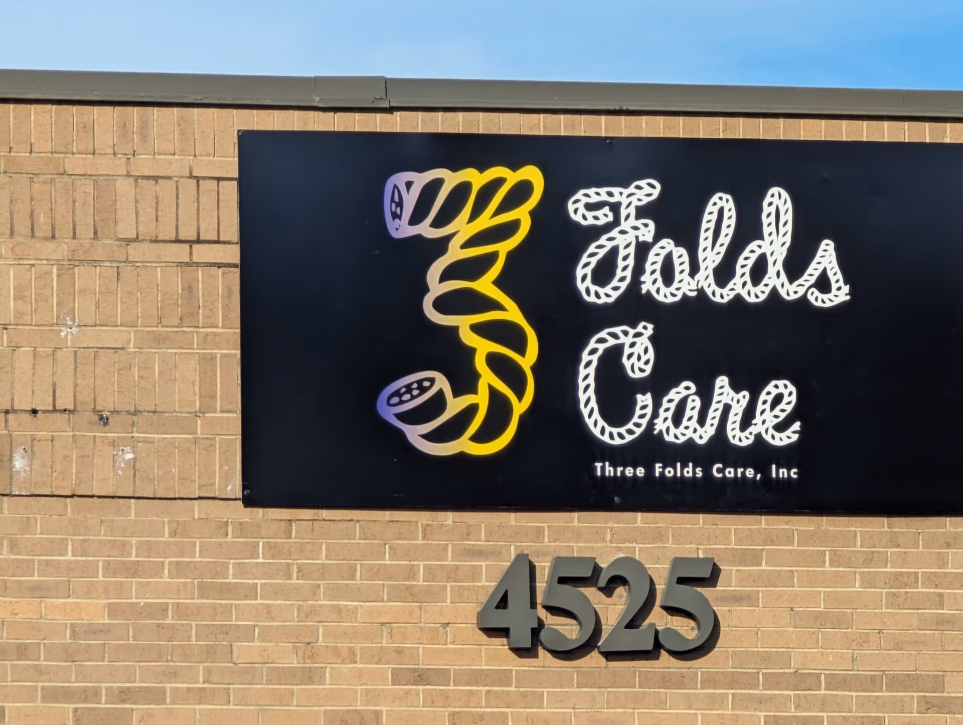 Exterior brick wall with a large black sign reading Three Folds Care, Inc.