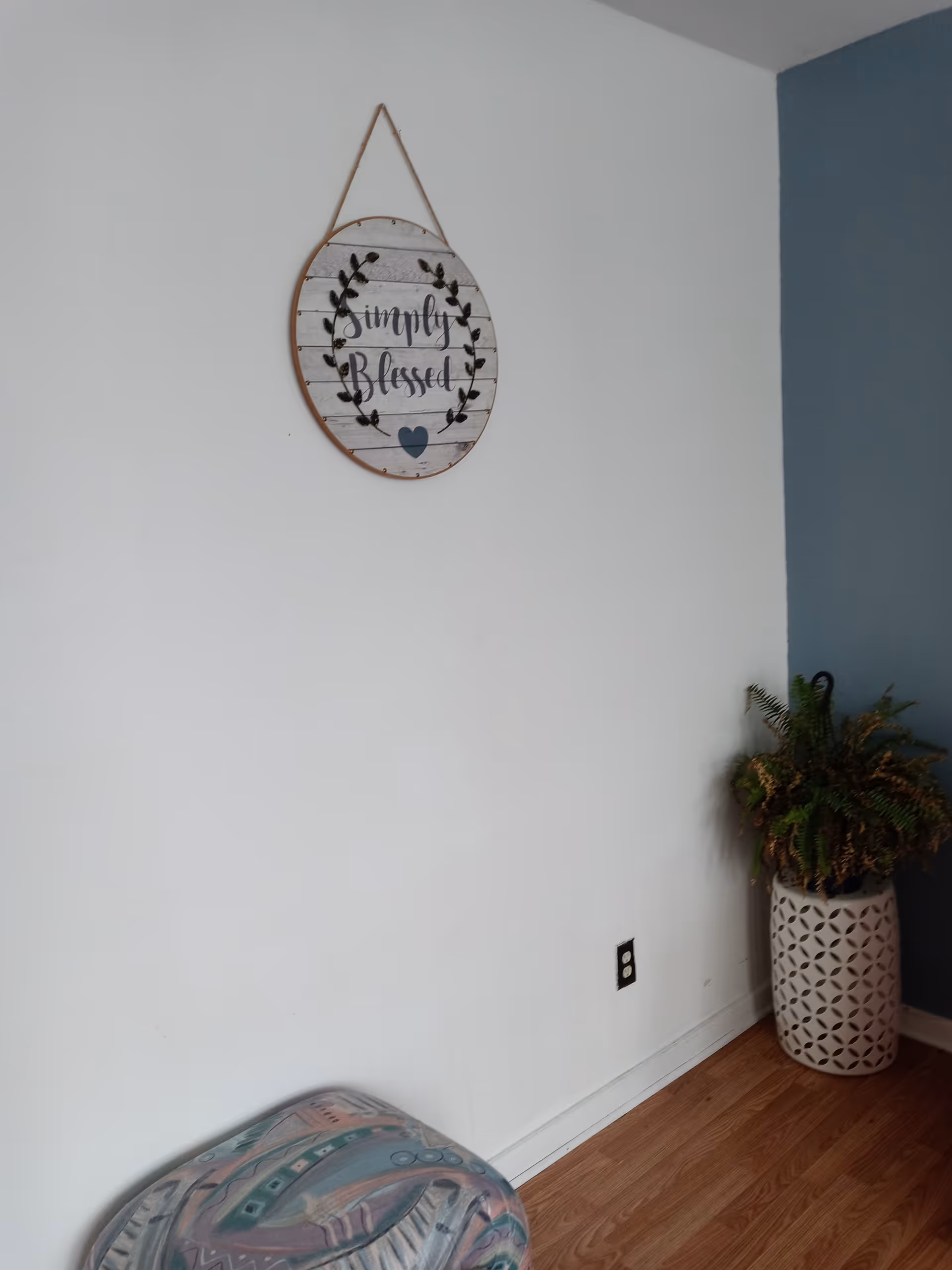 Corner of a living space with a decorative sign, potted plant, and ottoman.