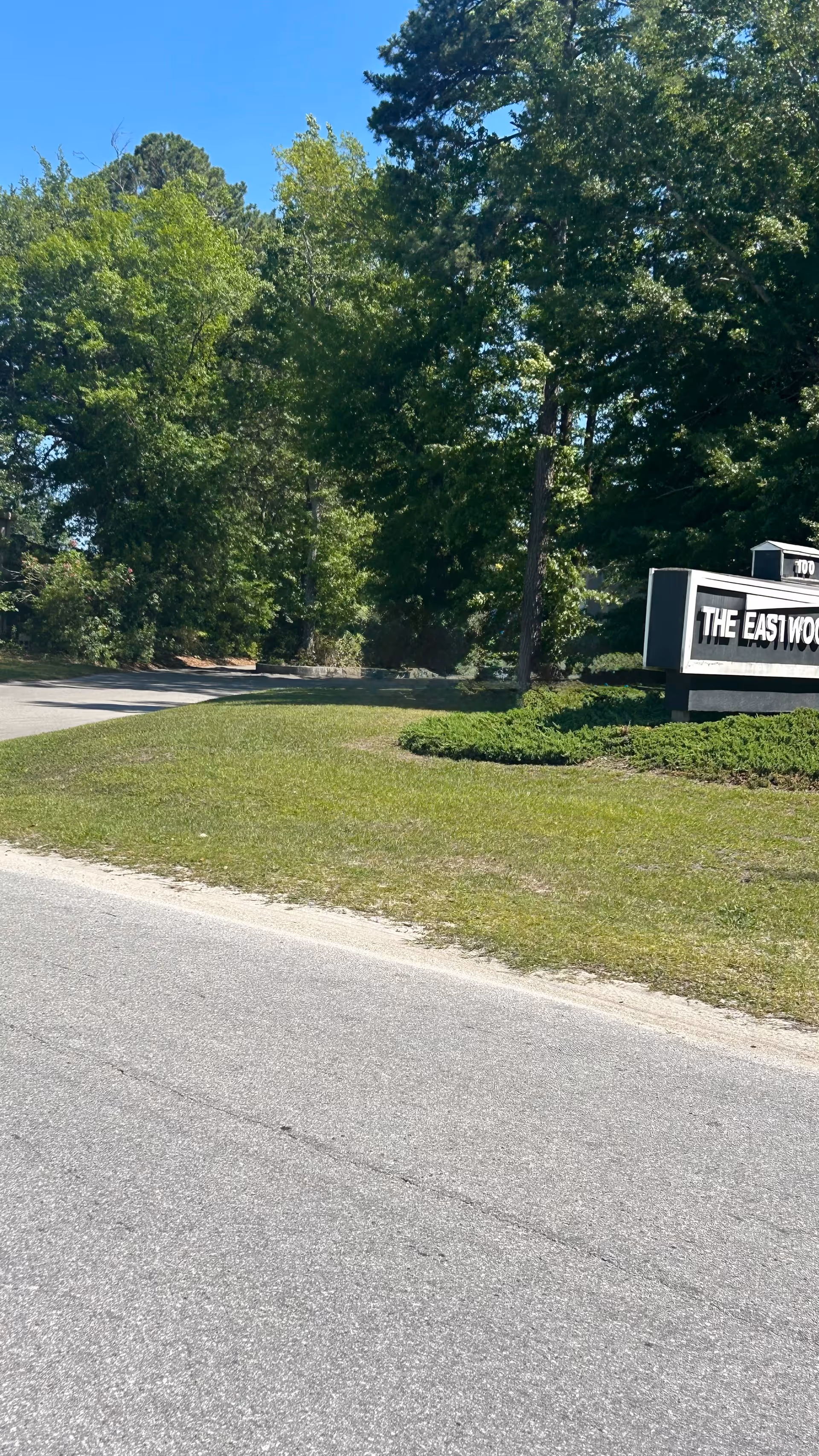 Tree-lined road with a large entrance sign visible near the curb.