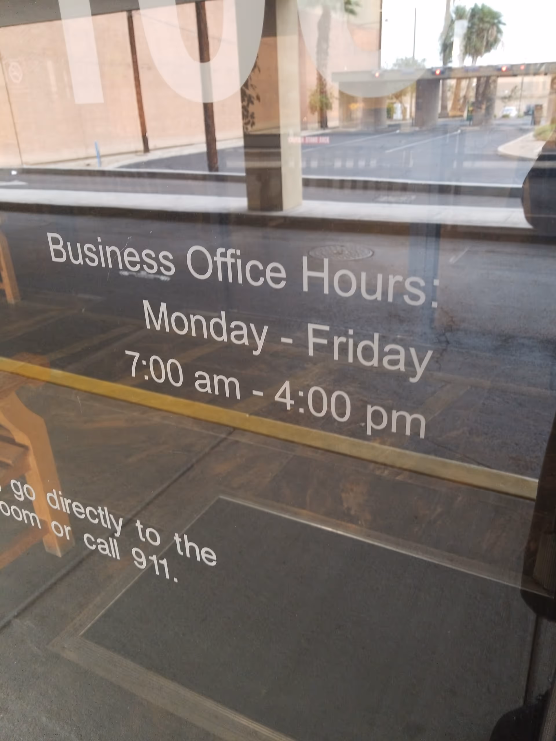 Glass entry door displays business office hours with street reflection outside.