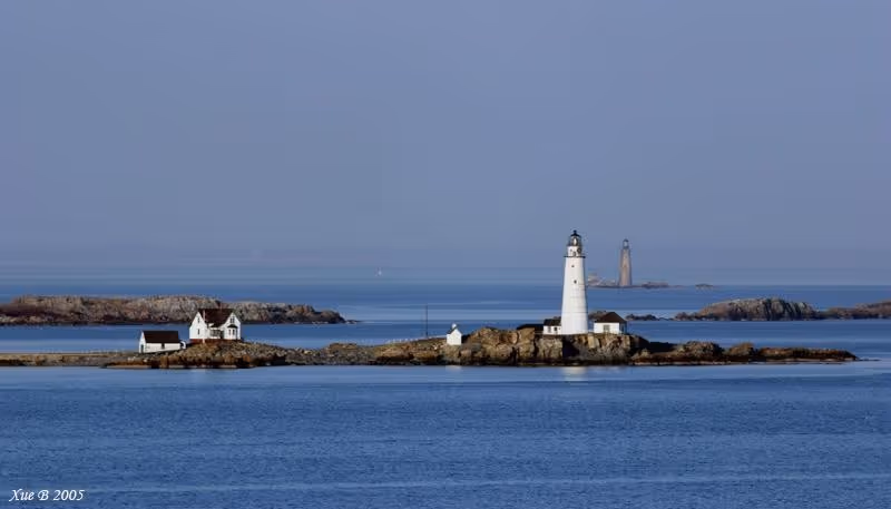 A small island with a white lighthouse and cottages surrounded by calm blue water.