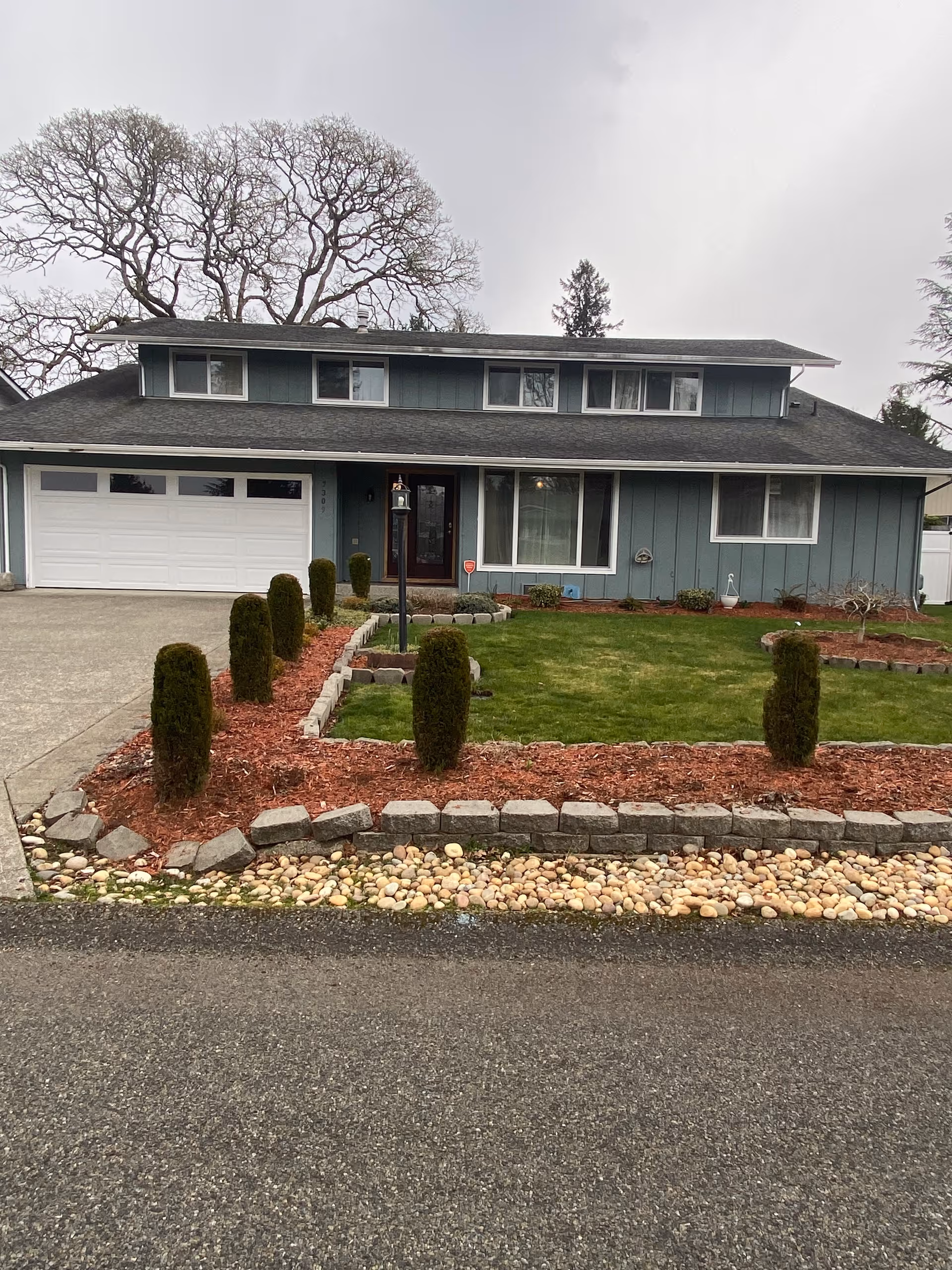 Front view of a blue two-story home with manicured lawn and stone-edged landscaping.